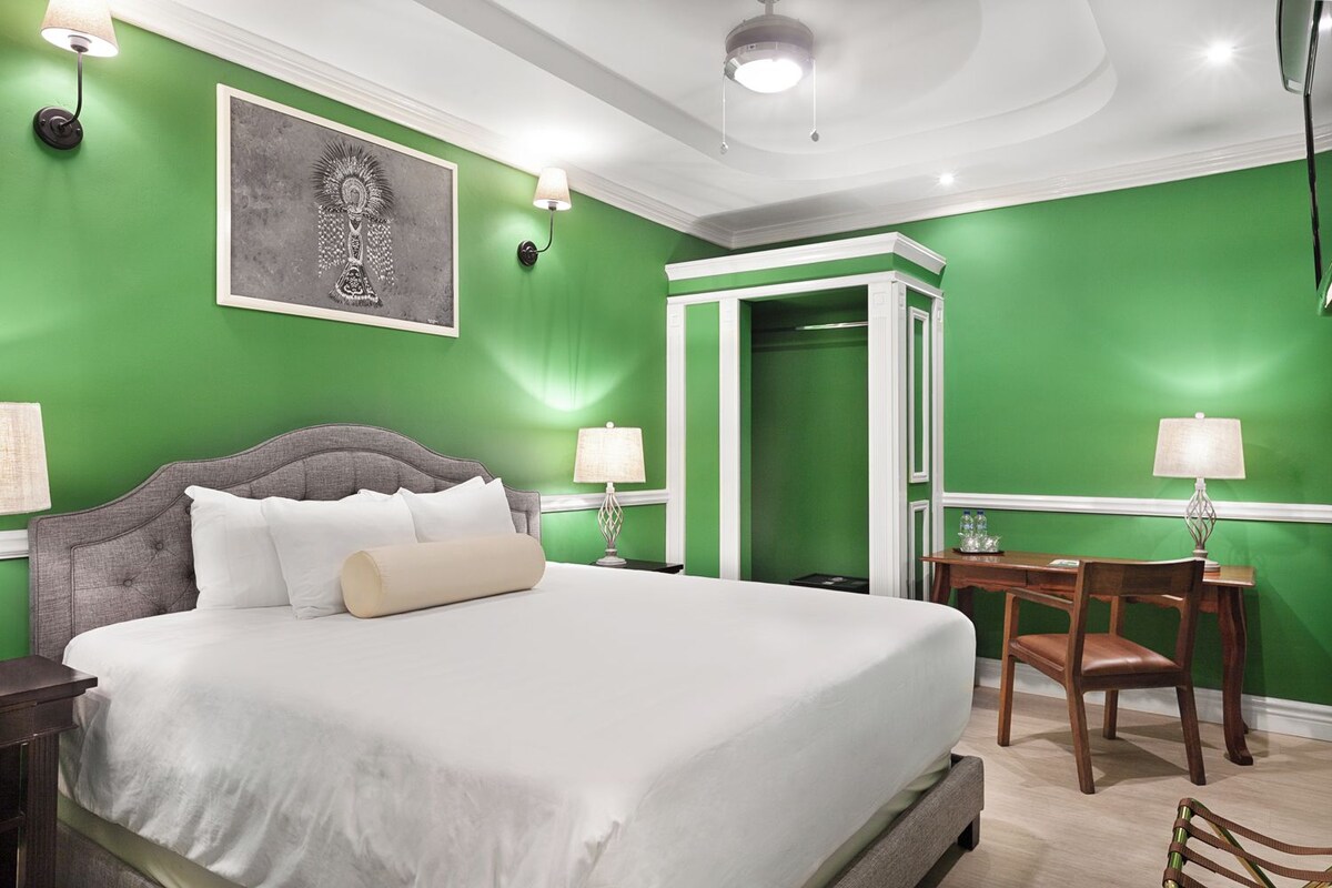 Habitación de hotel con una cama grande, un escritorio con silla y una pared de acento verde.