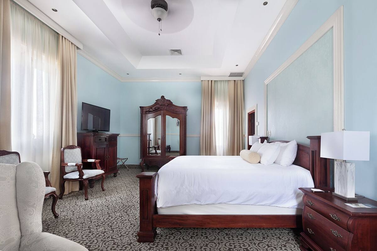 A hotel room with a large bed, a wooden dresser, a desk with a chair, a television, and a mirror.