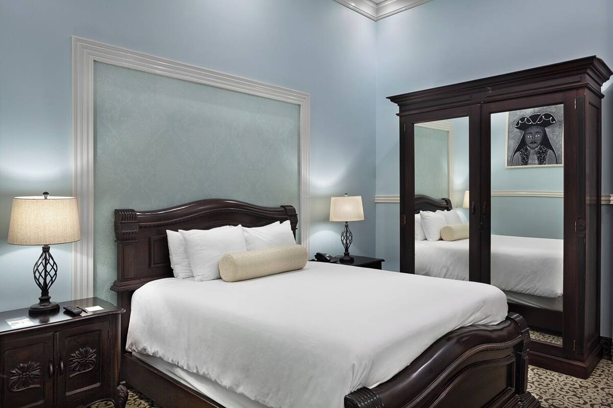 A neatly made bed with white linens, a dark wooden headboard, and two bedside lamps.