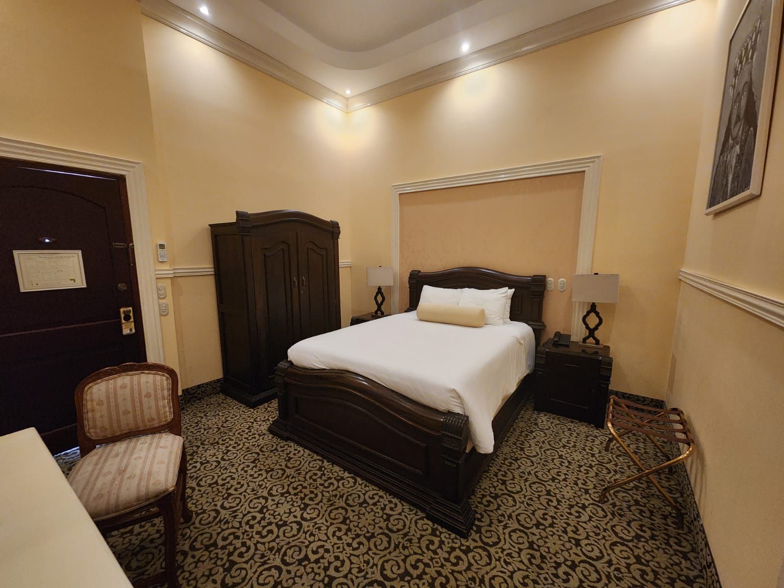 A hotel room with a large bed, a wardrobe, a desk, and a chair.