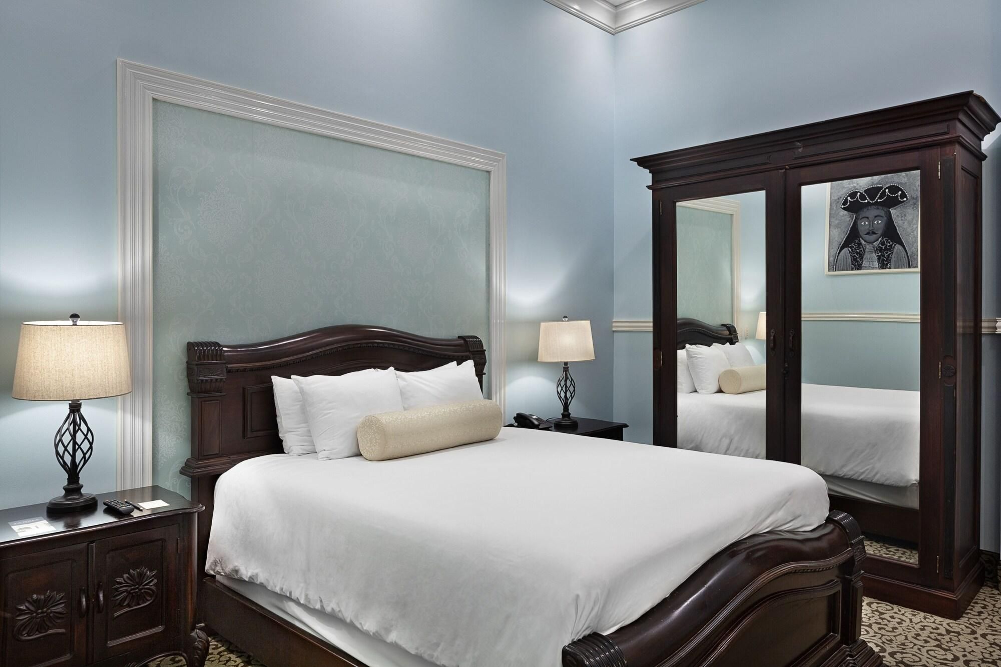 A bedroom with a large bed, two bedside tables, a nightstand, a mirror, and a wall with a decorative panel.
