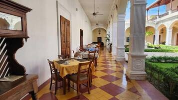 A corridor with a checkered floor, tables with chairs, and a ceiling fan.