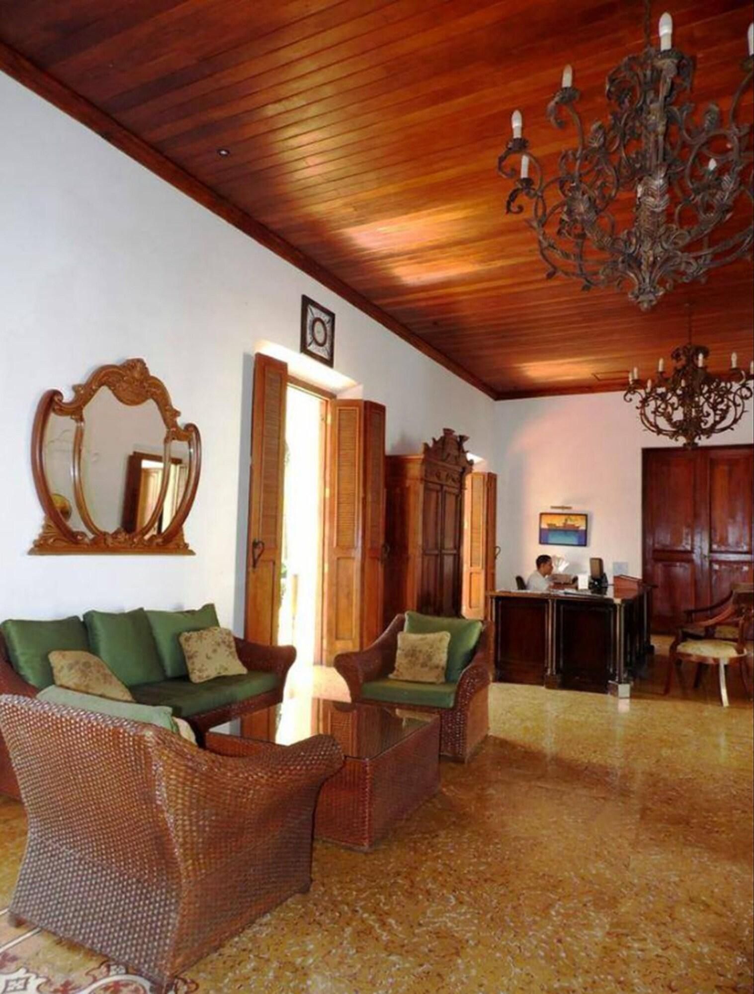 A room with a wooden ceiling, a chandelier, a mirror, a desk, and wicker furniture.