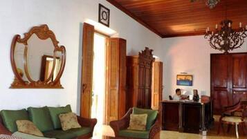 A room with a wooden ceiling, a chandelier, a mirror, a desk, and wicker furniture.