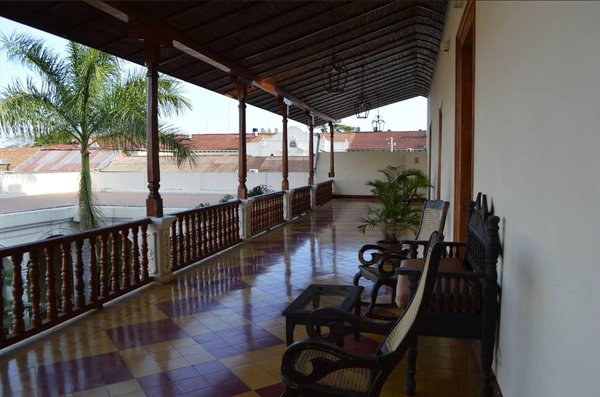 A balcony with a checkered floor, wooden railing, and two chairs.