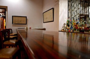 A bar area with a long wooden counter, two framed maps on the wall, and a bar stocked with various bottles. - Hotel La Perla León (León)