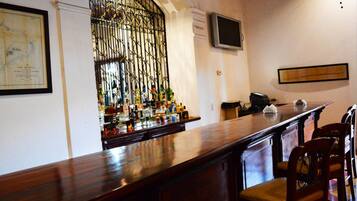A bar area with a wooden counter, bar stools, a television mounted on the wall, and a decorative metal gate.