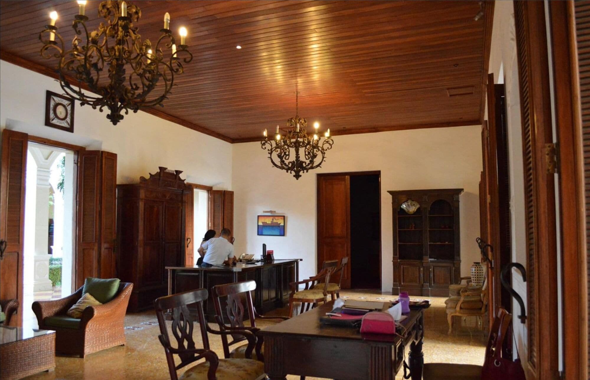 Amplia habitación con techo de madera, candelabro, mesa de comedor con sillas, aparador de madera y estantería.