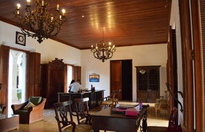 A spacious room with a wooden ceiling, a chandelier, a dining table with chairs, a wooden cabinet, and a bookshelf. - Hotel La Perla León (León)