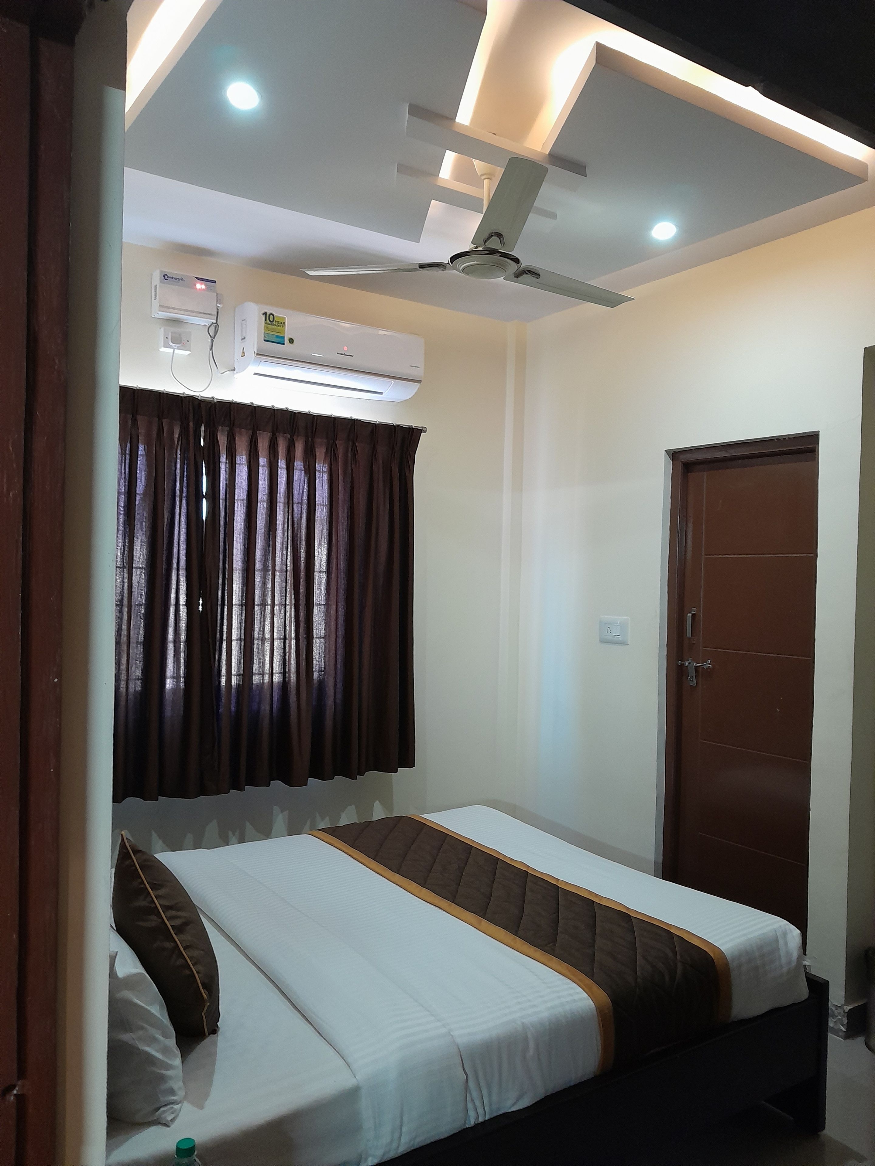 A bedroom with a bed, an air conditioning unit, a ceiling fan, and a door.