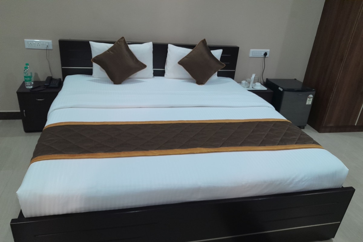 Habitación de hotel con una cama grande, una mesita de noche con un teléfono y una botella, y un cubo de basura pequeño.
