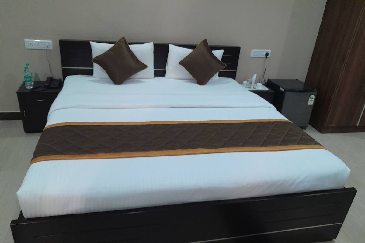 Ein Hotelzimmer mit einem großen Bett, einem Nachttisch mit Telefon und Flasche sowie einer kleinen Mülltonne.