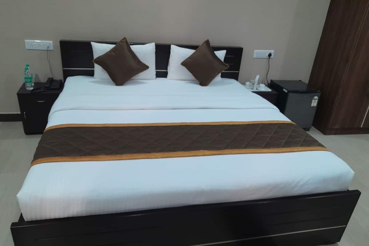 Quarto de hotel com uma cama grande, uma mesa de cabeceira com um telefone e uma garrafa, e uma pequena lixeira.