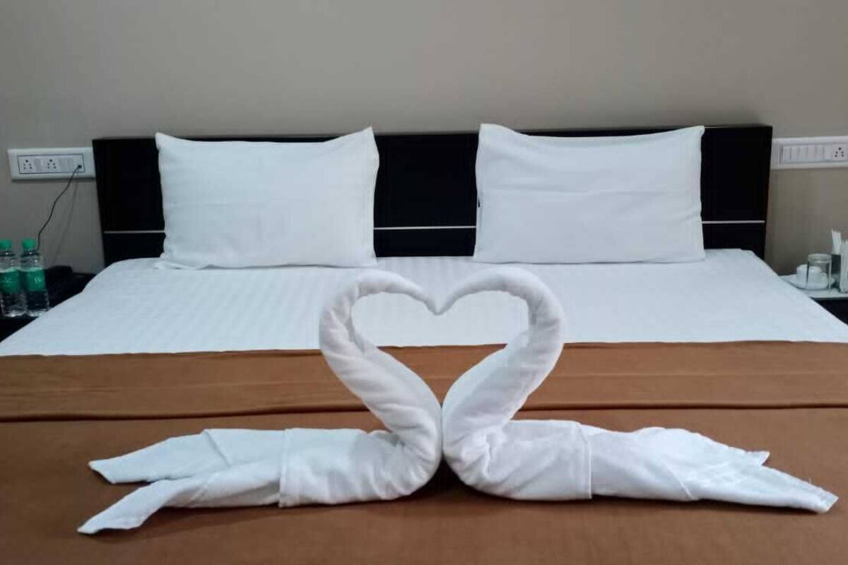 Ein Hotelzimmer mit einem ordentlich bezogenen Bett, zwei weißen Kissen, einer braunen Bettdecke und einer herzförmigen Handtuchgestaltung auf dem Bett.