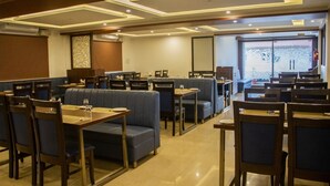 A hotel dining area with booths and tables, ceiling lights, and a large window. - The Nisarga Grand Bangalore India (Bengaluru)
