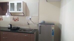 Una cocina con refrigerador, hervidor, pileta y un mueble con espejo.