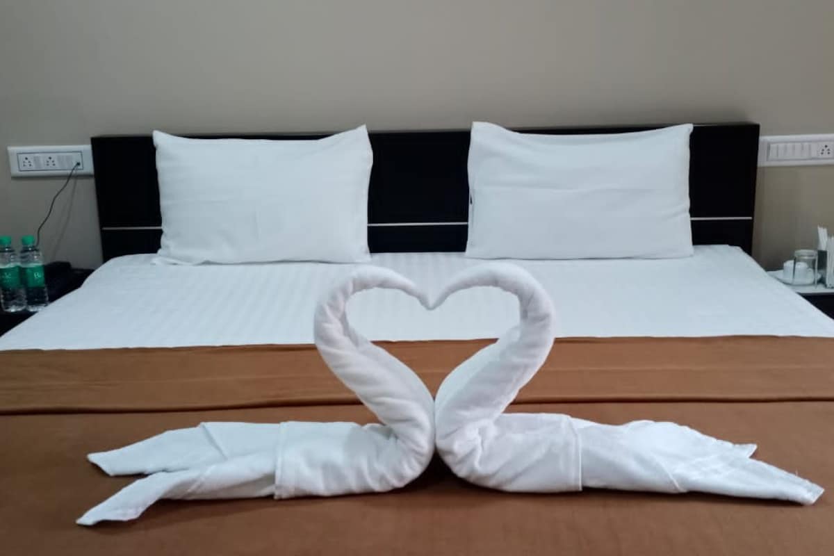 Habitación de hotel con una cama bien hecha, dos almohadas blancas, una colcha marrón y un arreglo de toallas con forma de corazón sobre la cama.