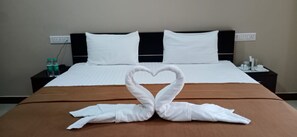 A hotel room with a neatly made bed, two white pillows, a brown bedspread, and a heart-shaped towel arrangement on the bed. - The Nisarga Grand Bangalore India (Bengaluru)