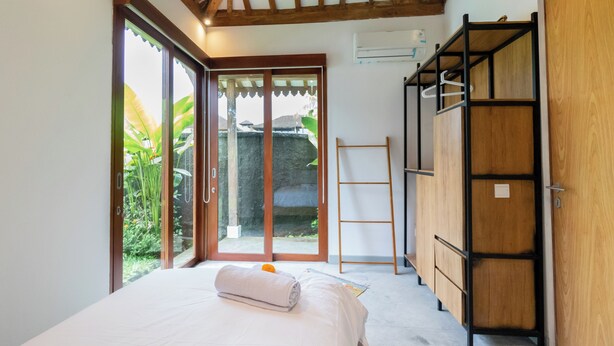 Une chambre à coucher comprenant un lit, une armoire en bois, une échelle et une porte-fenêtre coulissante donnant sur un espace extérieur.