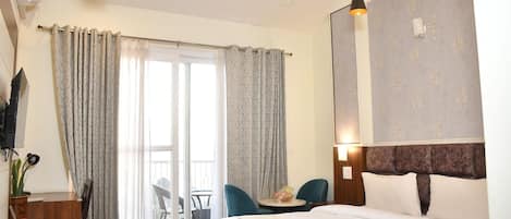 A hotel room with a bed, a desk, a chair, a table, a ceiling fan, and a sliding glass door.