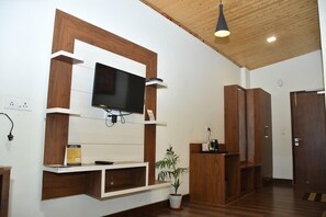Una sala de estar moderna con un televisor montado, estanterías de madera, una planta en maceta y una puerta.