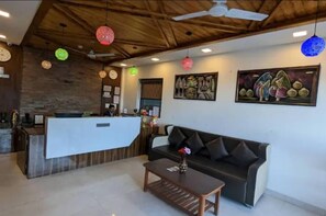 A reception area with a reception desk, a black sofa, a coffee table, and a ceiling fan.