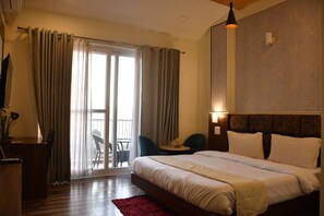 A hotel room with a bed, a desk, a chair, a red rug, and a view through the window. - Hotel Le Halcyon Kasau (Solan)