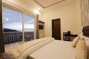 A hotel room with a bed, a desk, a chair, a TV, and a balcony with a view. - Hotel Le Halcyon Kasau (Solan)