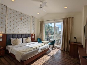 A hotel room with a bed, a desk, a chair, a balcony with a view, and a ceiling fan. - Hotel Le Halcyon Kasau (Solan)
