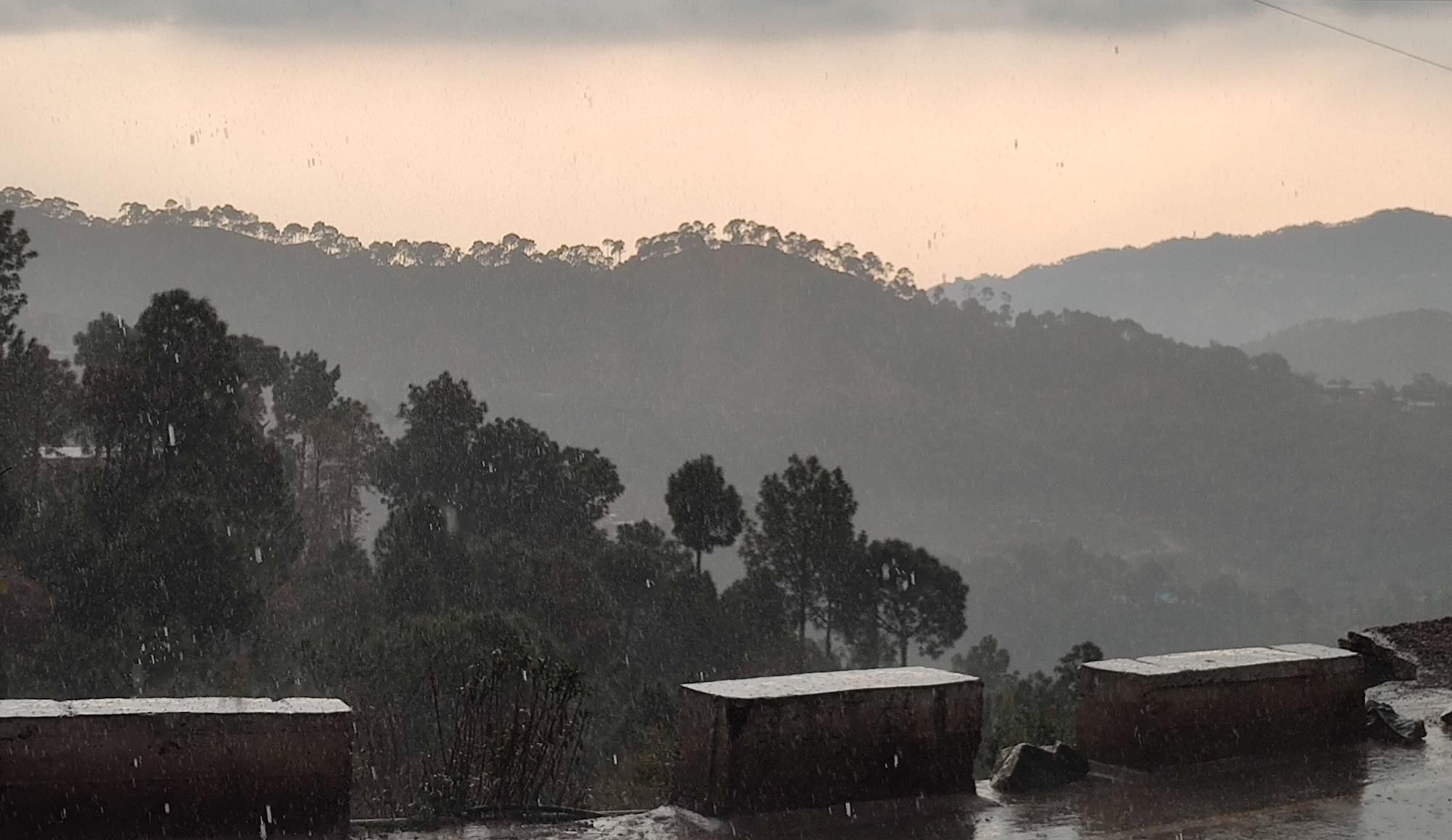 A rural landscape with hills, trees, and a building with a sloped roof.