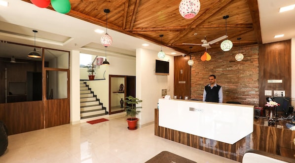 A reception area with a wooden ceiling, a reception desk, a staircase, and a potted plant. - Hotel Le Halcyon Kasau (Solan)