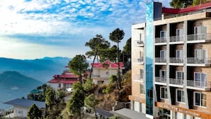 A hotel with multiple balconies, a view of the sea, and a mountainous backdrop. - Hotel Le Halcyon Kasau (Solan)