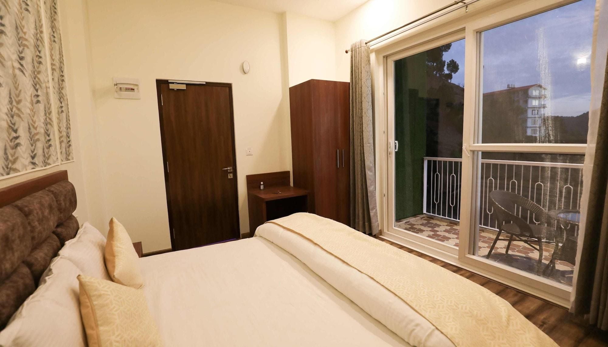 Habitació d'hotel amb llit, armari, taula petita, cadira i un balcó amb vistes.