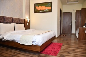 A bedroom with a wooden bed, a red rug, a painting on the wall, and a wooden wardrobe. - Hotel Le Halcyon Kasau (Solan)