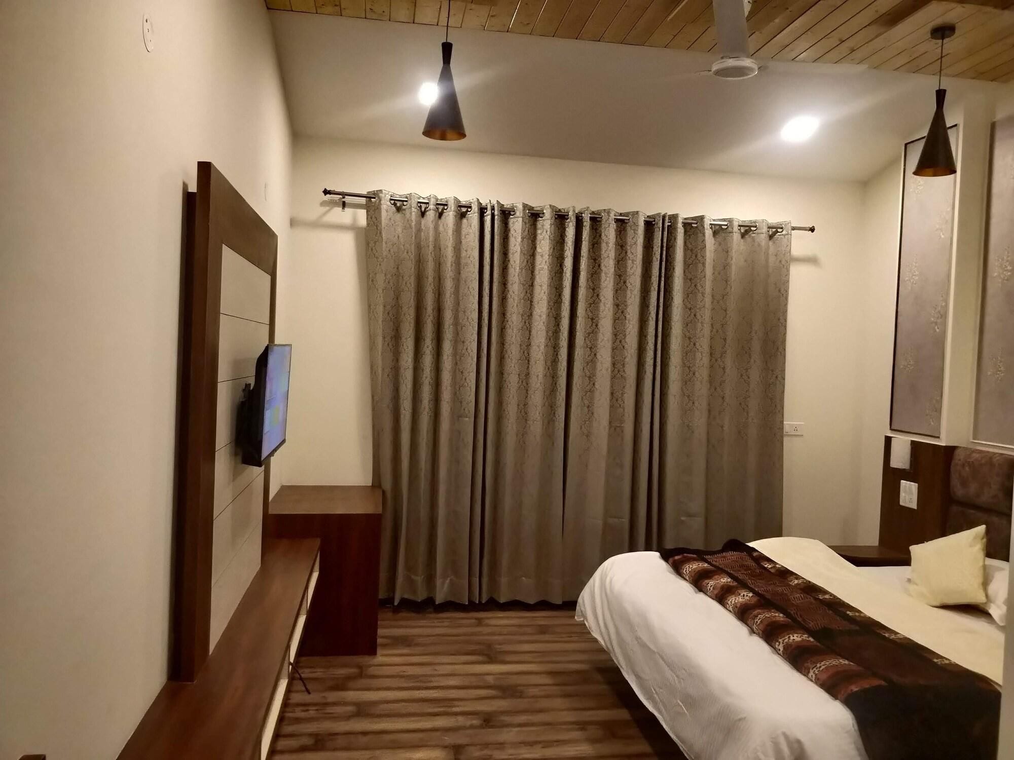 Une chambre d’hôtel avec un lit, un téléviseur fixé au mur, un banc en bois et un rideau.
