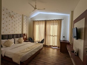 A hotel room with a bed, a desk, a chair, a television, and a ceiling fan. - Hotel Le Halcyon Kasau (Solan)