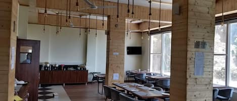A restaurant with wooden walls and ceiling, hanging light fixtures, a bar area, and tables with chairs.