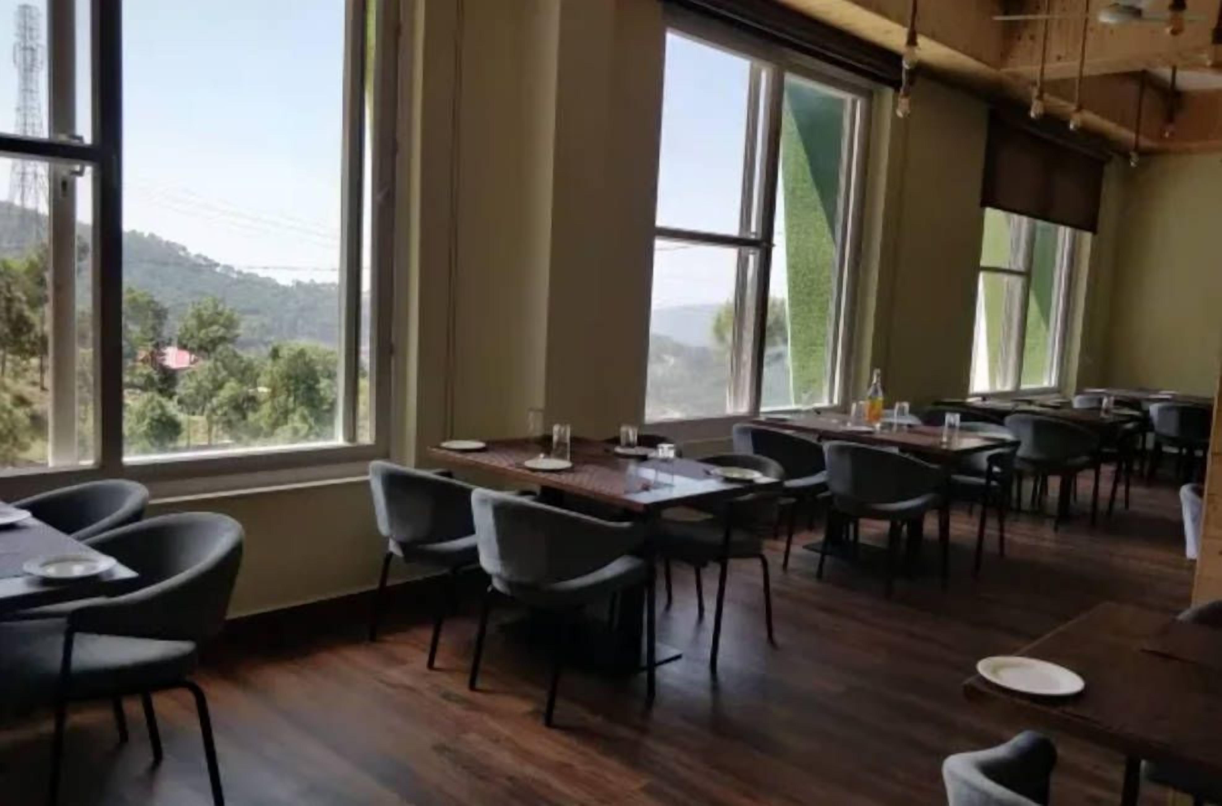 A restaurant with multiple tables and chairs, large windows with a view of greenery and hills.