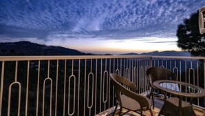 A balcony with wicker chairs and a table, overlooking a mountainous landscape at dusk. - Hotel Le Halcyon Kasau (Solan)