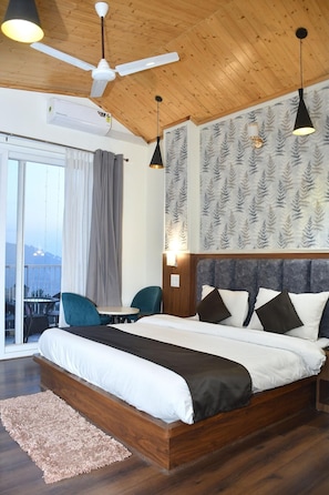 A bedroom with a large bed, a ceiling fan, a window with curtains, and a view of the city. - Hotel Le Halcyon Kasau (Solan)