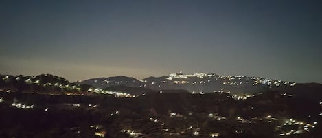 Vista nocturna de un paisaje urbano con edificios iluminados y colinas al fondo.