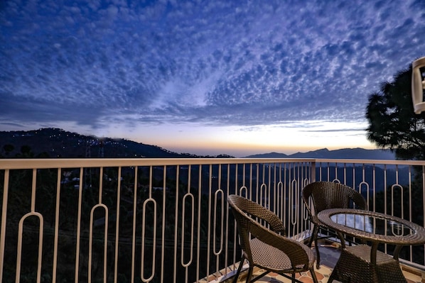 A balcony with wicker chairs and a table, overlooking a mountainous landscape at dusk. - Hotel Le Halcyon Kasau (Solan)