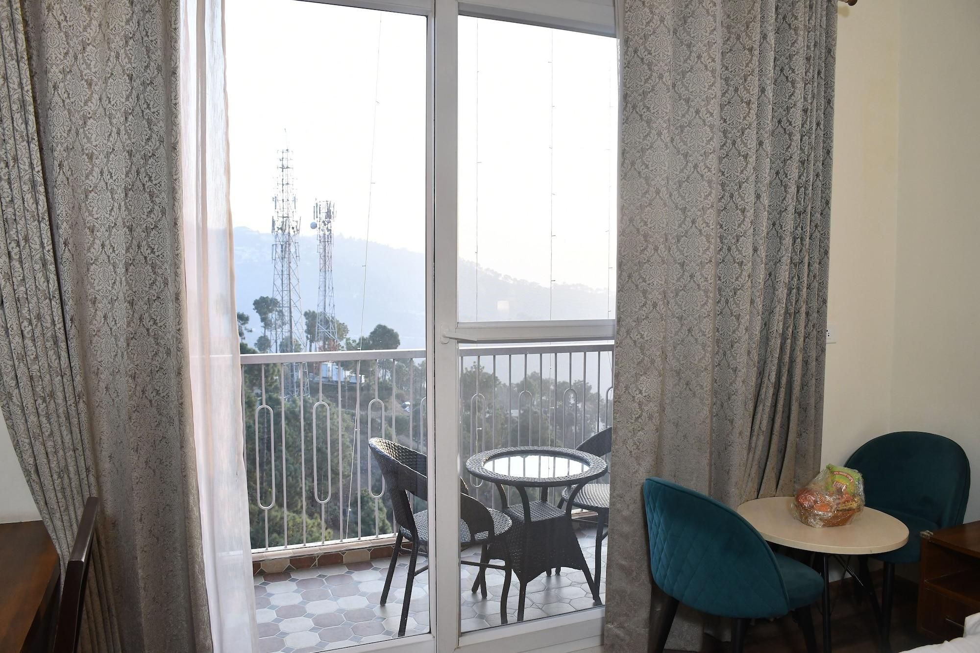 A balcony with a table and chairs, a view of the cityscape, and patterned curtains.