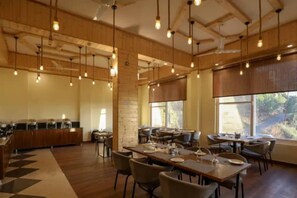 A spacious dining area with wooden tables and chairs, a buffet setup, and large windows allowing natural light. - Hotel Le Halcyon Kasau (Solan)