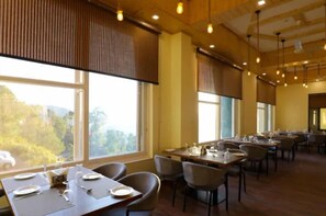 A dining area with tables set for service, large windows with blinds, and a view of the outdoors. - Hotel Le Halcyon Kasau (Solan)