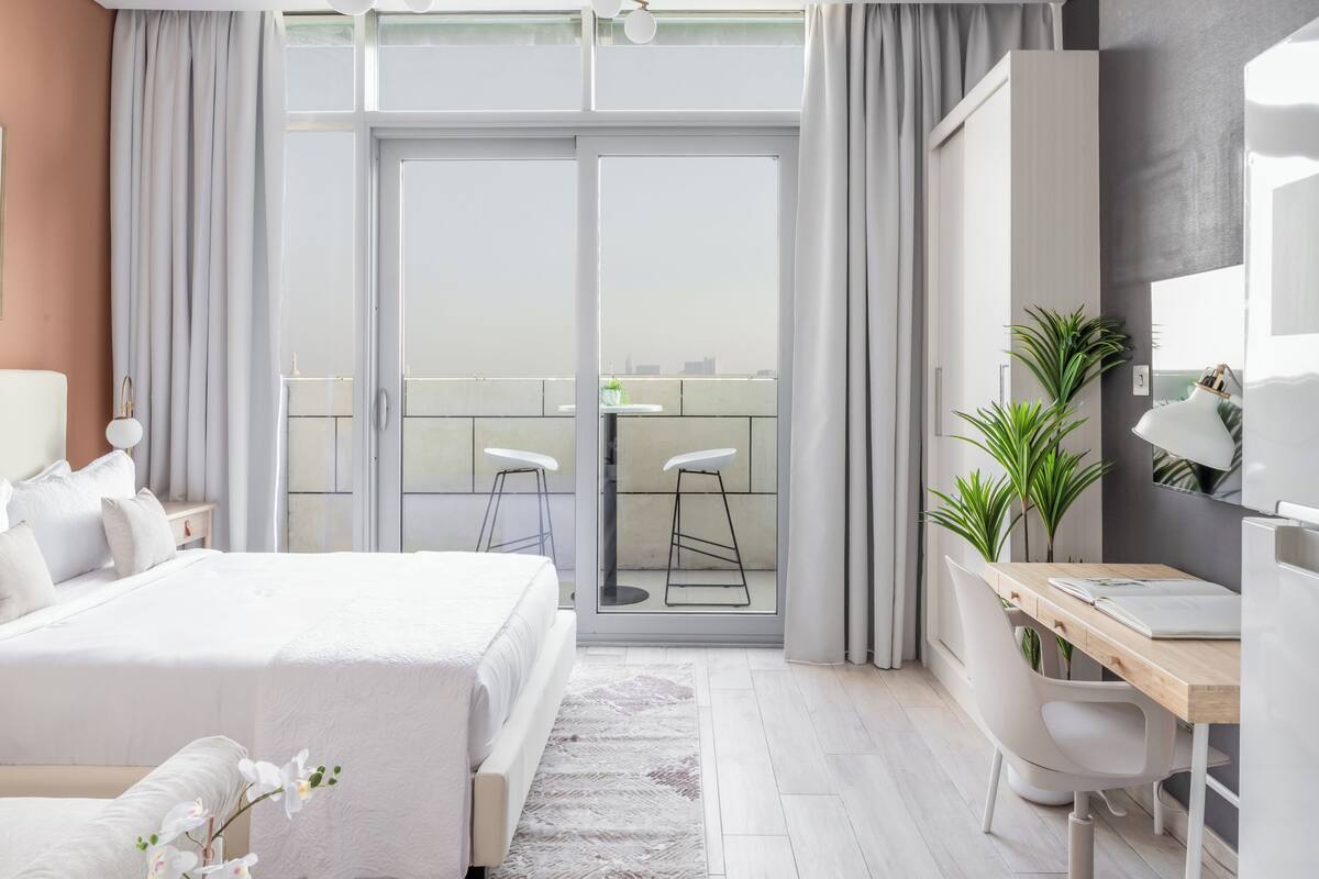 A modern hotel room with a bed, desk, and balcony.