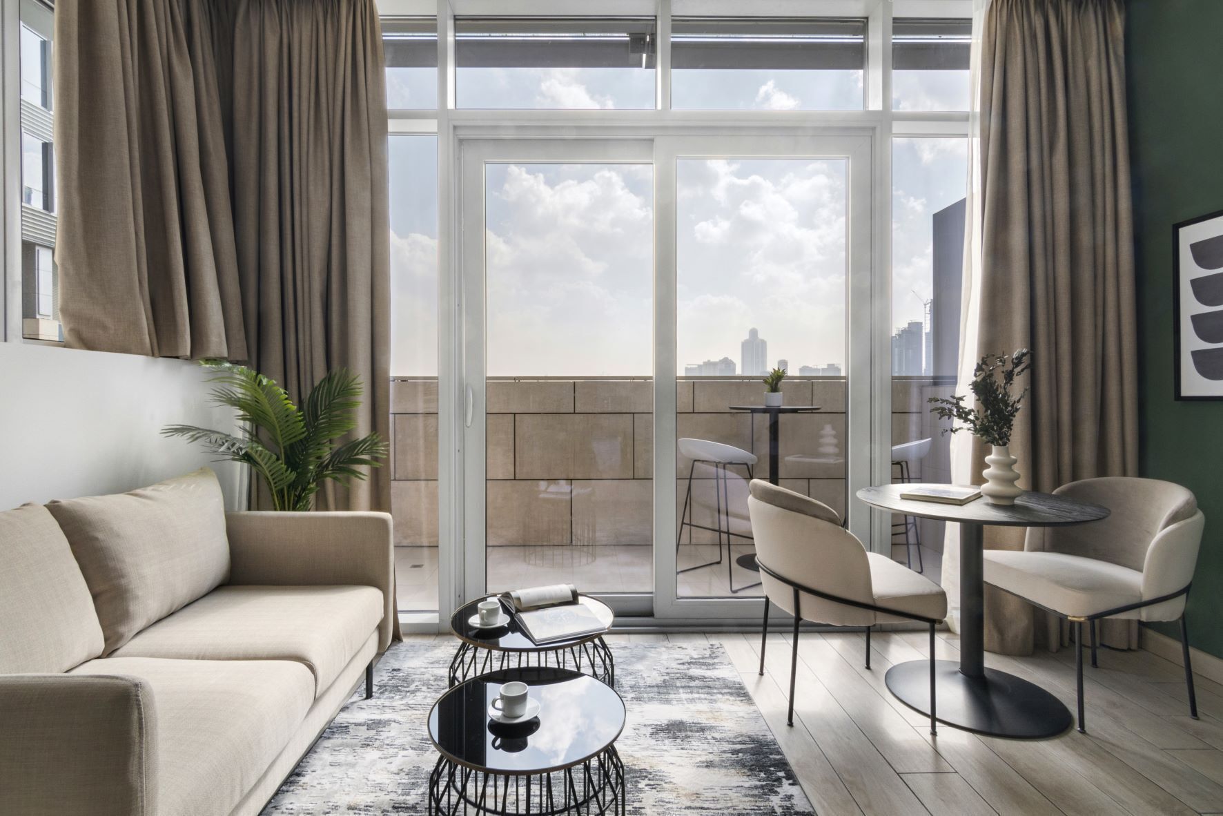 Ein modernes Wohnzimmer mit Sofa, Couchtisch und Sesseln, ein Balkon mit Blick auf die Stadt und ein Blumentopf.