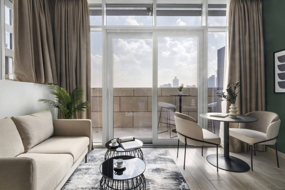 A modern living room with a sofa, coffee table, and chairs, a balcony with a city view, and a potted plant.