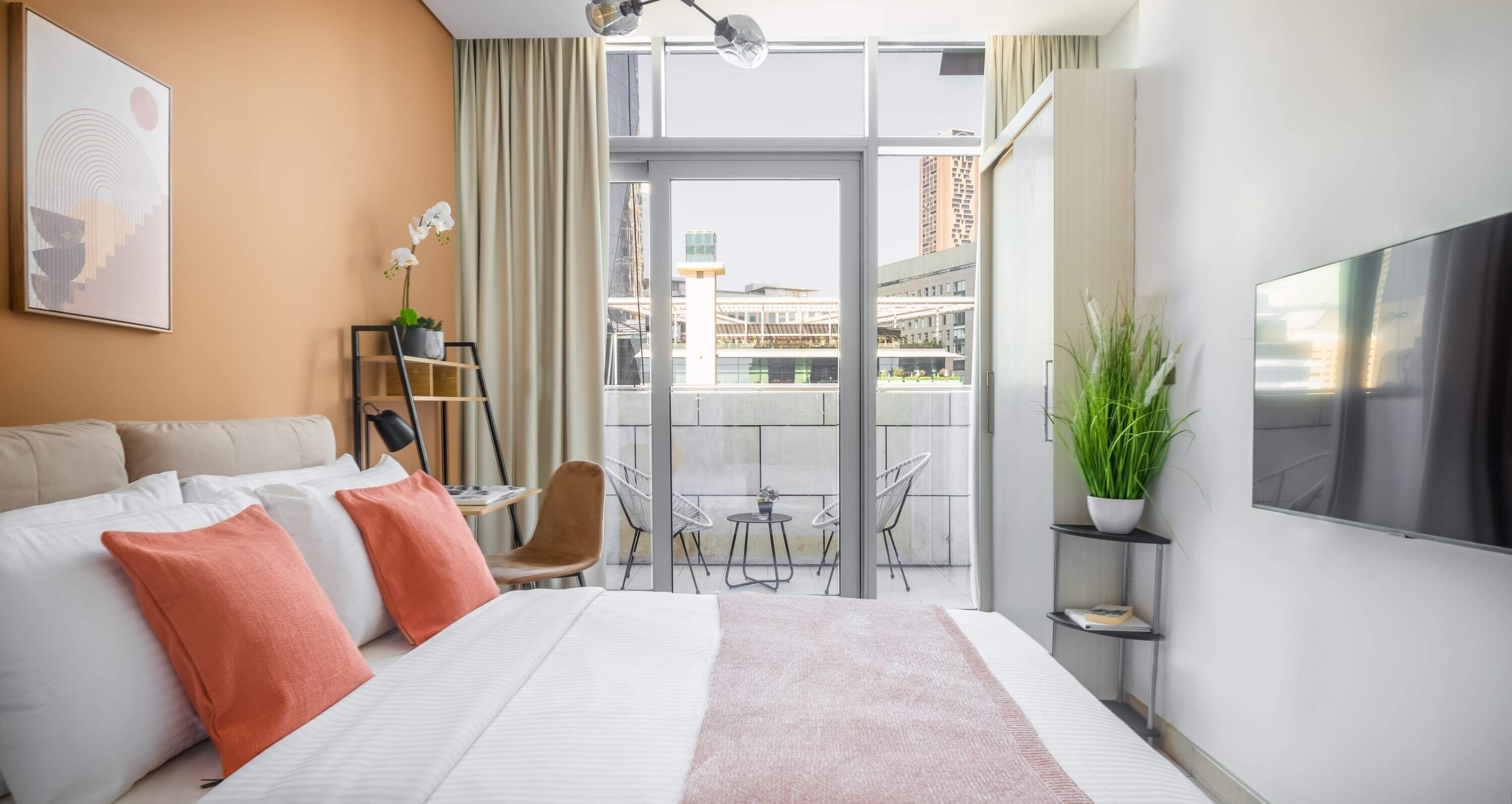 Ein modernes Hotelzimmer mit einem großen Bett, einem Fernseher, einem Balkon mit Blick auf die Stadt und einer Pflanze auf dem Nachttisch.