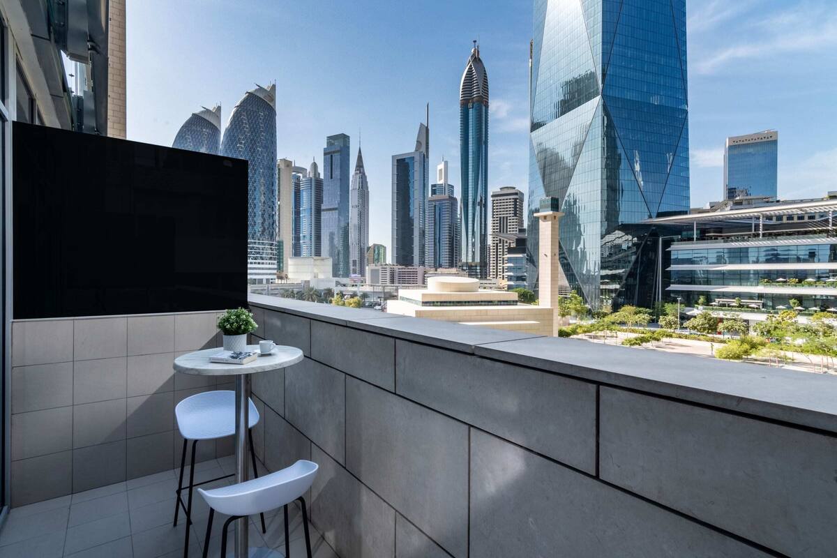 A modern urban balcony with a cityscape view, featuring contemporary buildings and a small seating area with a table and chairs.